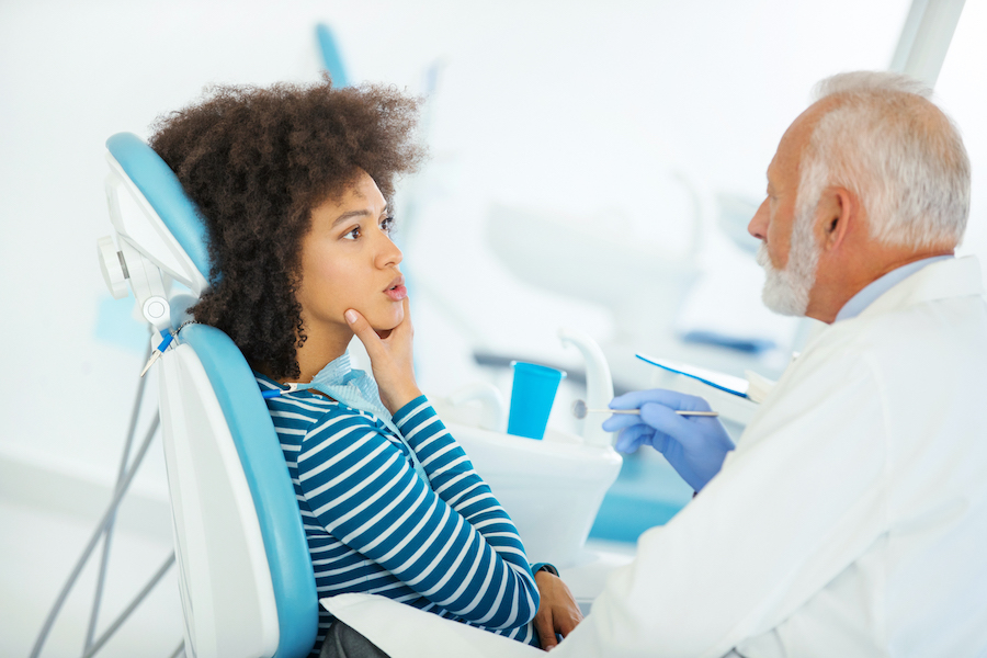 Curly-haired Black woman touches her jaw as her white older dentist explains a procedure to her at dentist in hermitage