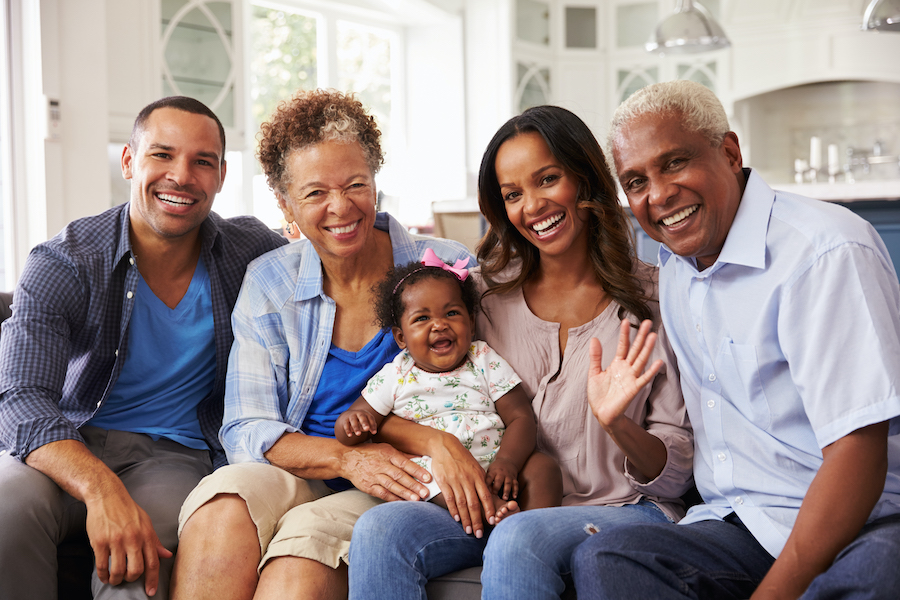 Black parents, daughter, and grandparents sit on the couch and smile before visiting their family dentist