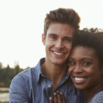 Black and white couple smile as they embrace outside