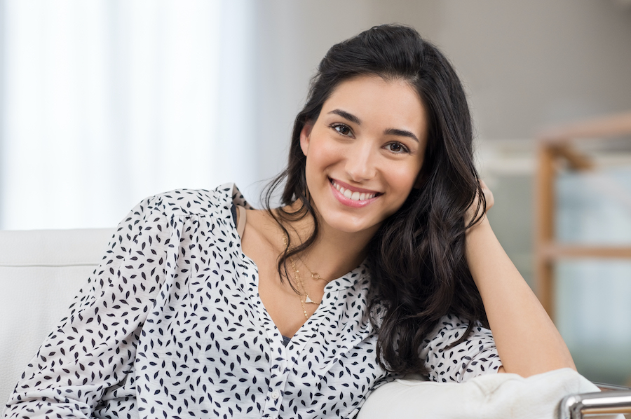 Smiling dark-haired woman in a black and white blouse leans on her elbow on the couch at dentist in hermitage