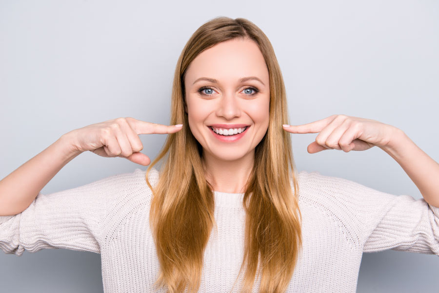 A smiling woman pointing to her white smile with the pointer finger on both hands. at dentist in hermitage