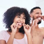 couple flossing their teeth together, caring for dental implants