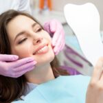 Patient admiring results of cosmetic dentistry in handheld mirror in dentist’s chair.