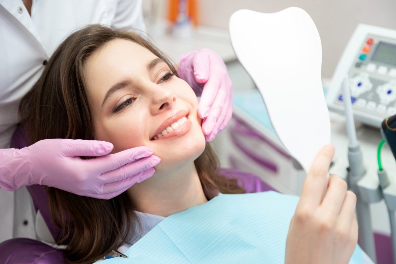 Patient admiring results of cosmetic dentistry in handheld mirror in dentist’s chair.